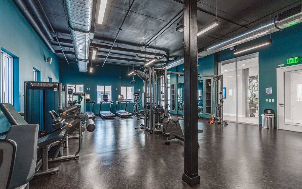 A gym with a variety of equipment and a green exit sign.
