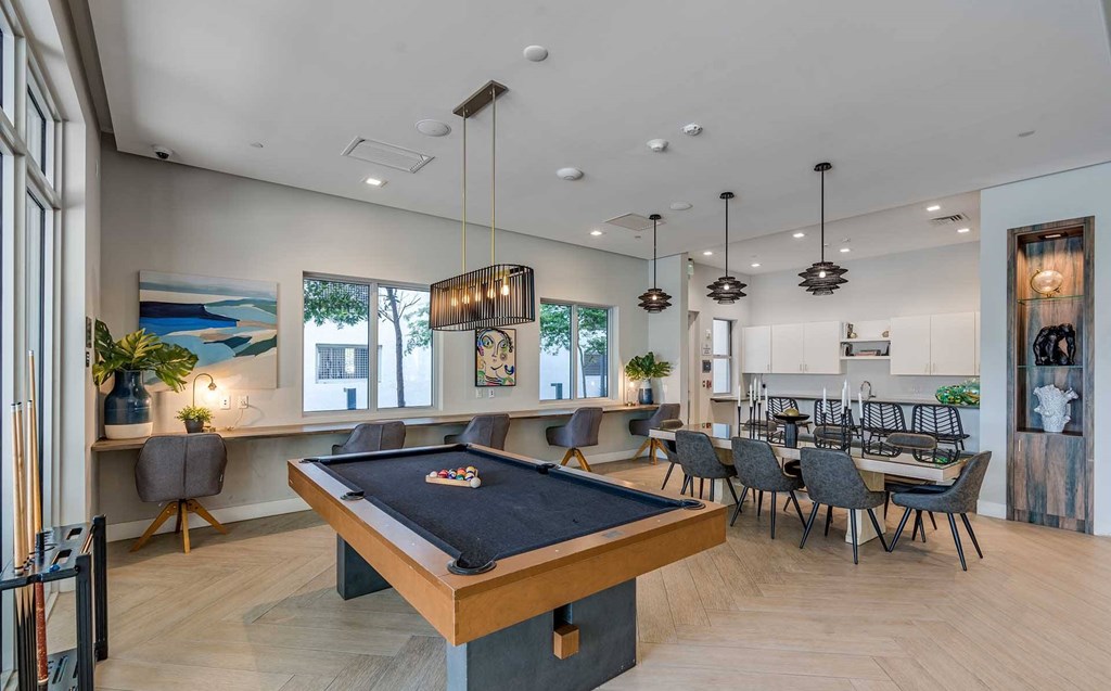 A pool table is in the middle of a room with a bar and a dining table.