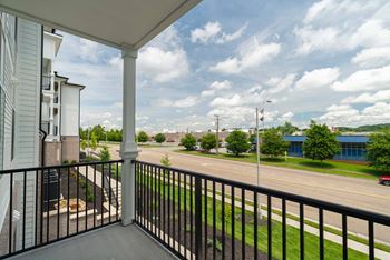 A balcony overlooks a street with a red car and buildings in the distance.