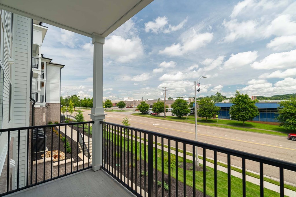 A balcony overlooks a street with a red car and buildings in the distance.