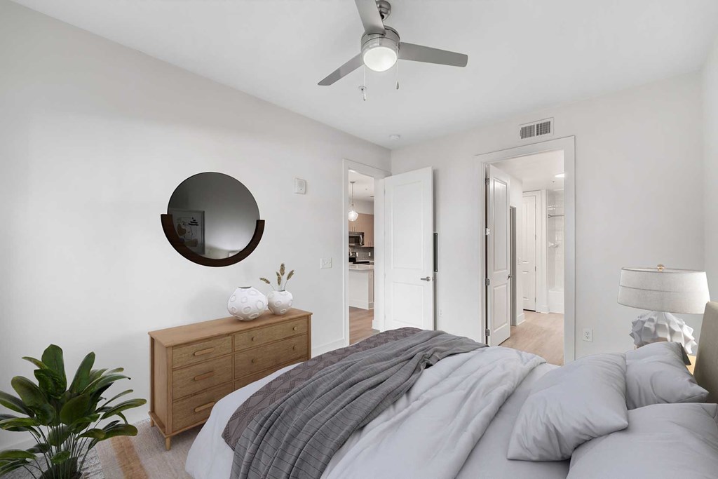 Decatur, GA Apartments Near Emory Hospital - ARLO - Spacious Bedroom With Vinyl Plank Flooring, Large Bed, Nightstand With Lamp, Dresser, Ceiling Fan, And Attached Bathroom.