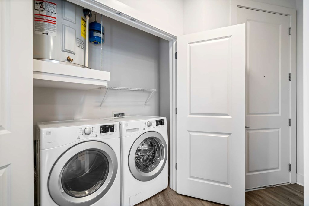A white door is open to reveal a laundry room with a washer and dryer.