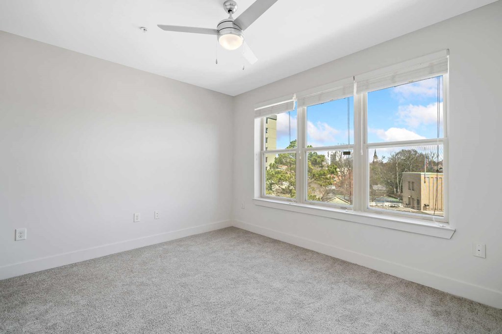 A room with a ceiling fan and a window overlooking a cityscape.