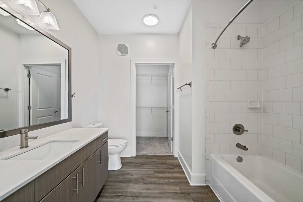 A white bathroom with a wooden floor and a white tub.