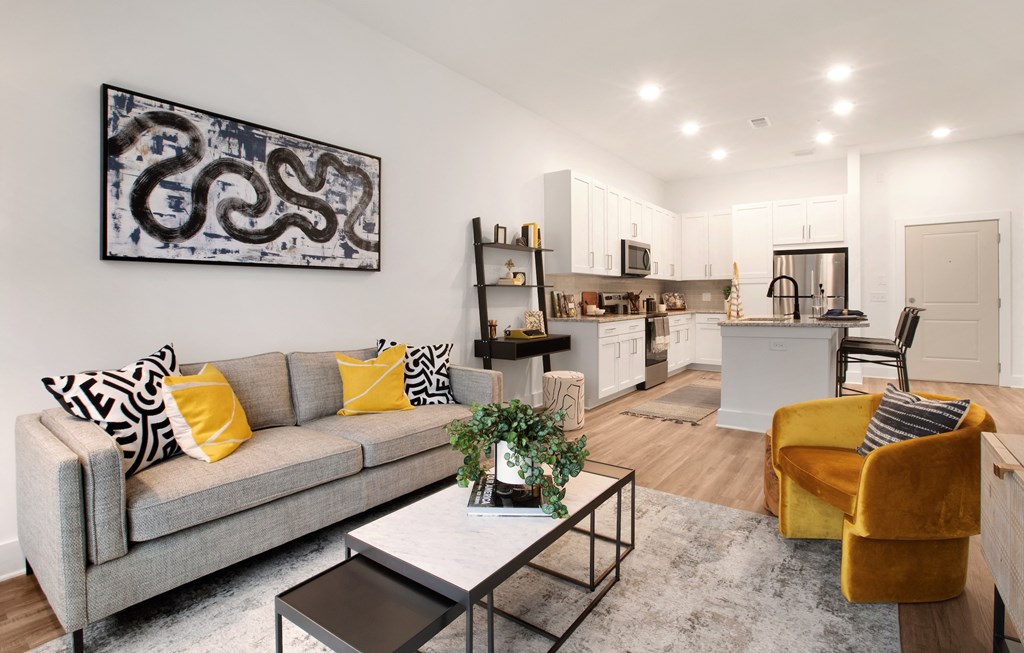 a living room with a couch coffee table and chair and a kitchen in the background
