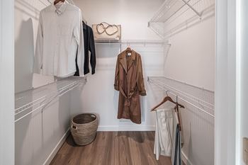 A white closet with clothes hanging and a basket on the floor