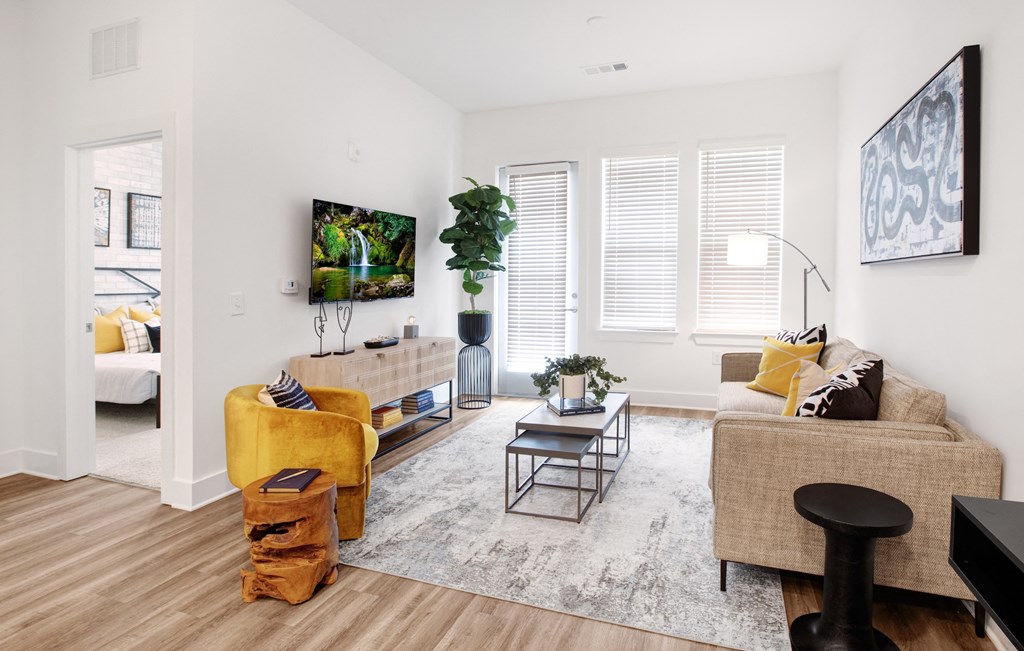 Apartments for Rent in Norcross GA - The Darnell - Furnished Living Room with Sofa, Mounted TV and Monitor with Storage, Armchairs, Carpet, Side Tables, Lamps, Houseplant, and Windows