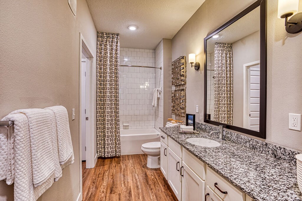 1-Bedroom Apartments in Maitland, FL - The Parker at Maitland Station - Bathroom with Wood Vinyl Plank Flooring, Double Sink Vanity, Granite Countertop, Wood-Tone Flat-Panel Cabinetry, and Tiled Shower/Tub Combo.