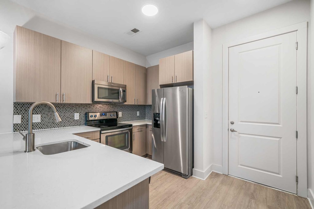 Decatur, GA Apartments Near Emory University- ARLO - Kitchen With Vinyl Plank Flooring, Stainless Steel Appliances, Quartz Countertops, Designer Tile Backsplash, And Wood-Tone Flat-Panel Cabinets.