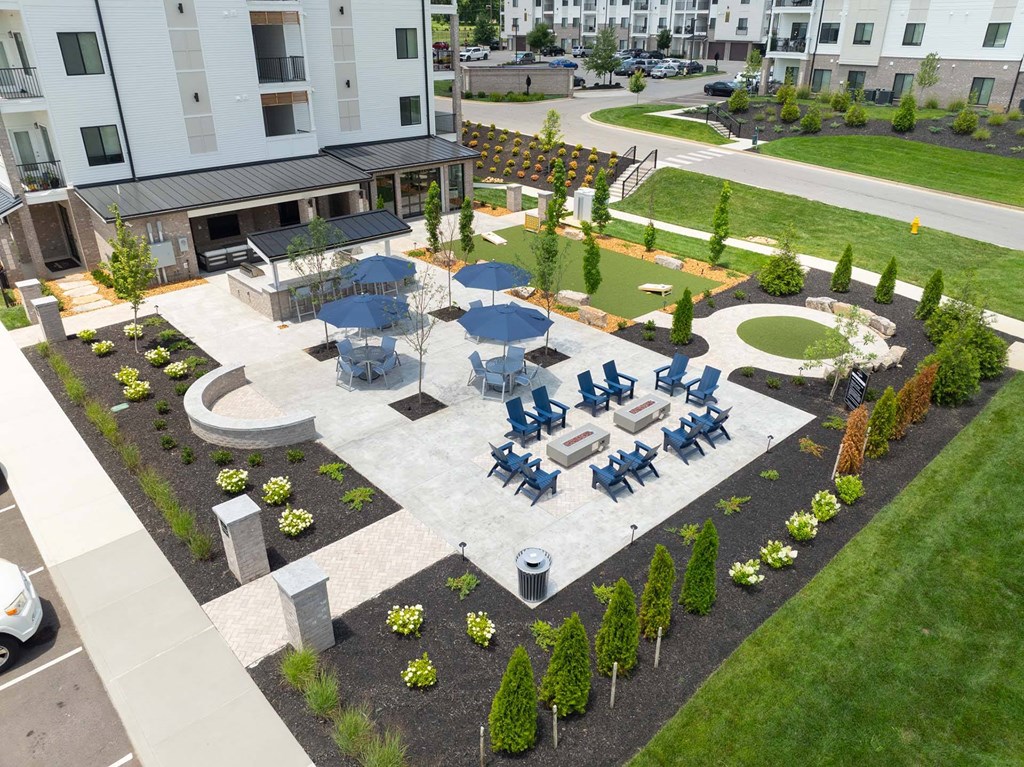 A large outdoor seating area with blue umbrellas and chairs is surrounded by a landscaped garden.