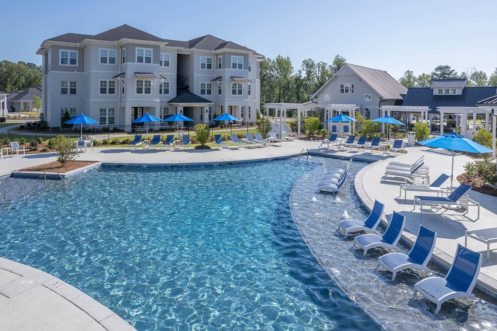 a swimming pool with chairs and umbrellas in front of an apartment building