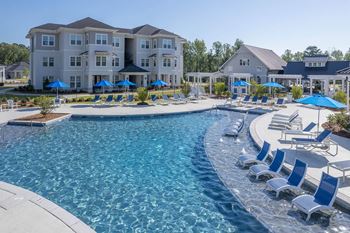 a swimming pool with chairs and umbrellas in front of an apartment building