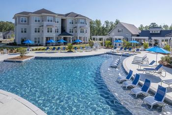 a swimming pool with chairs and umbrellas in front of an apartment building
