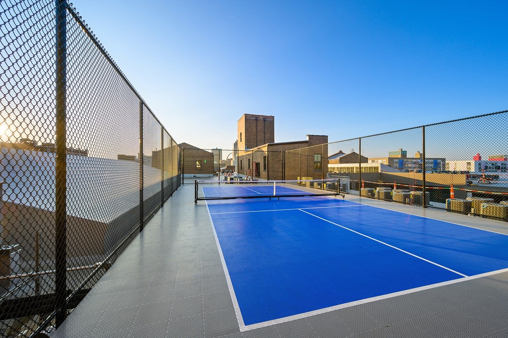a blue tennis court on a rooftop with a city in the background