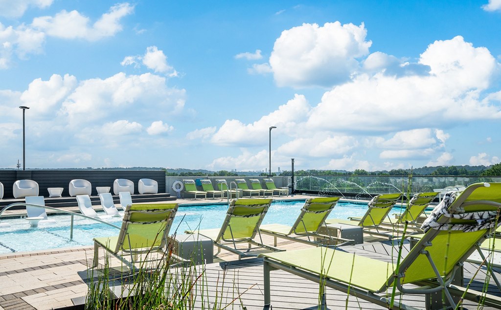 the pool on the top floor of the hotel with green chairs and a blue sky