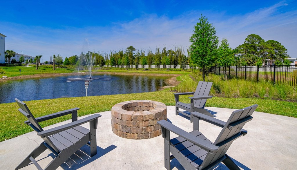 a patio with a fire pit and benches next to a pond