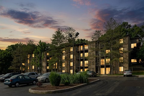 A parking lot with cars and a building with windows and trees in front.
