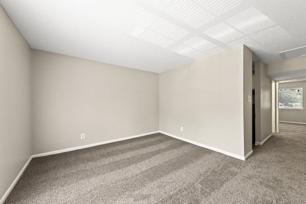 an empty living room with carpet and a door to a hallway