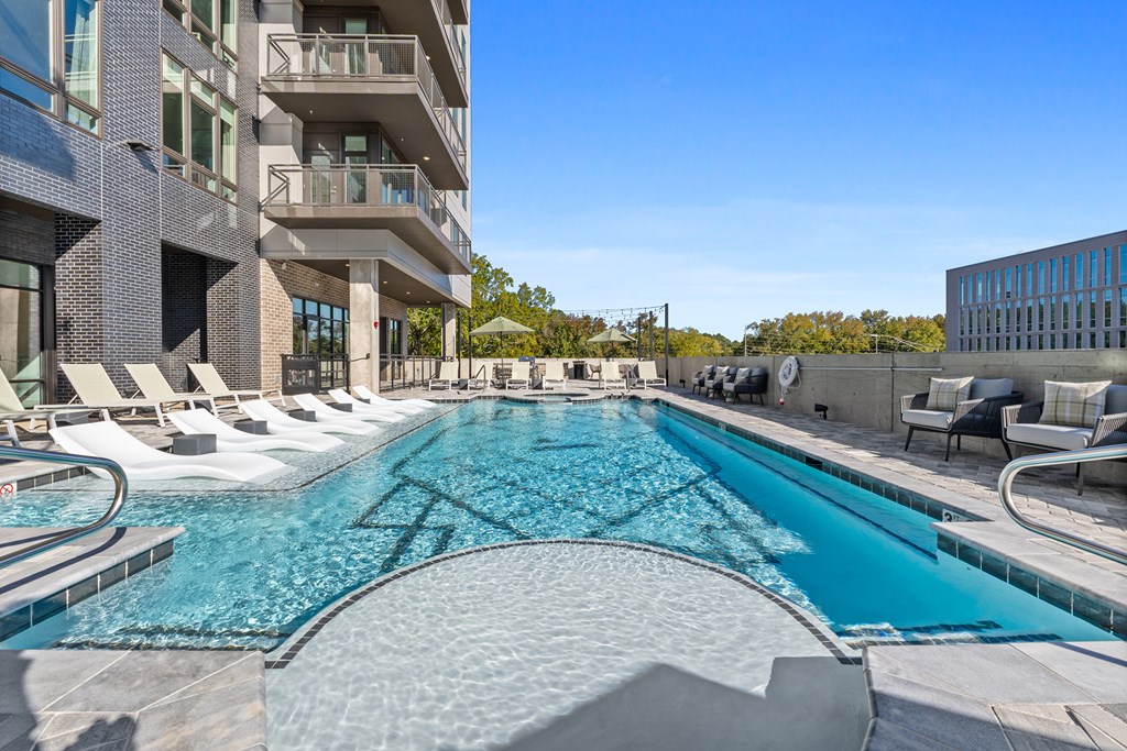 A large outdoor swimming pool surrounded by lounge chairs and buildings.