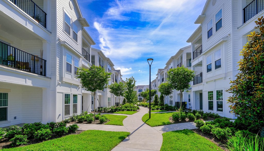 a walkway between two apartment buildings with green grass and trees