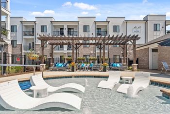 A pool area with a wooden pergola and lounge chairs.