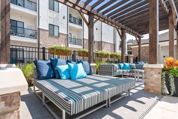 A patio with a striped cushion sofa and a wooden pergola.