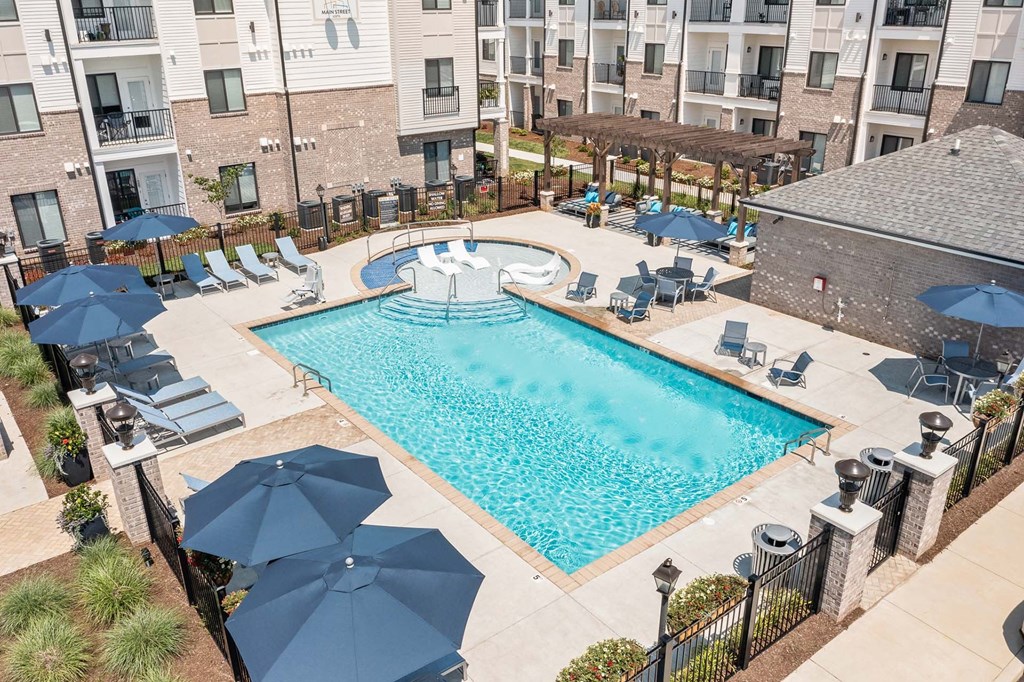 A large swimming pool surrounded by lounge chairs and umbrellas in a residential area.