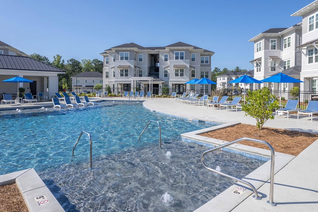 a large pool with blue umbrellas in front of an apartment building