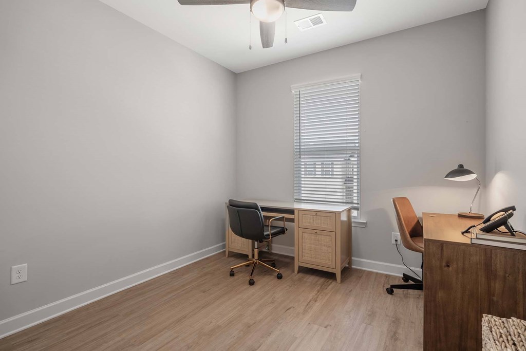 A room with a desk, chair, and a window with blinds.