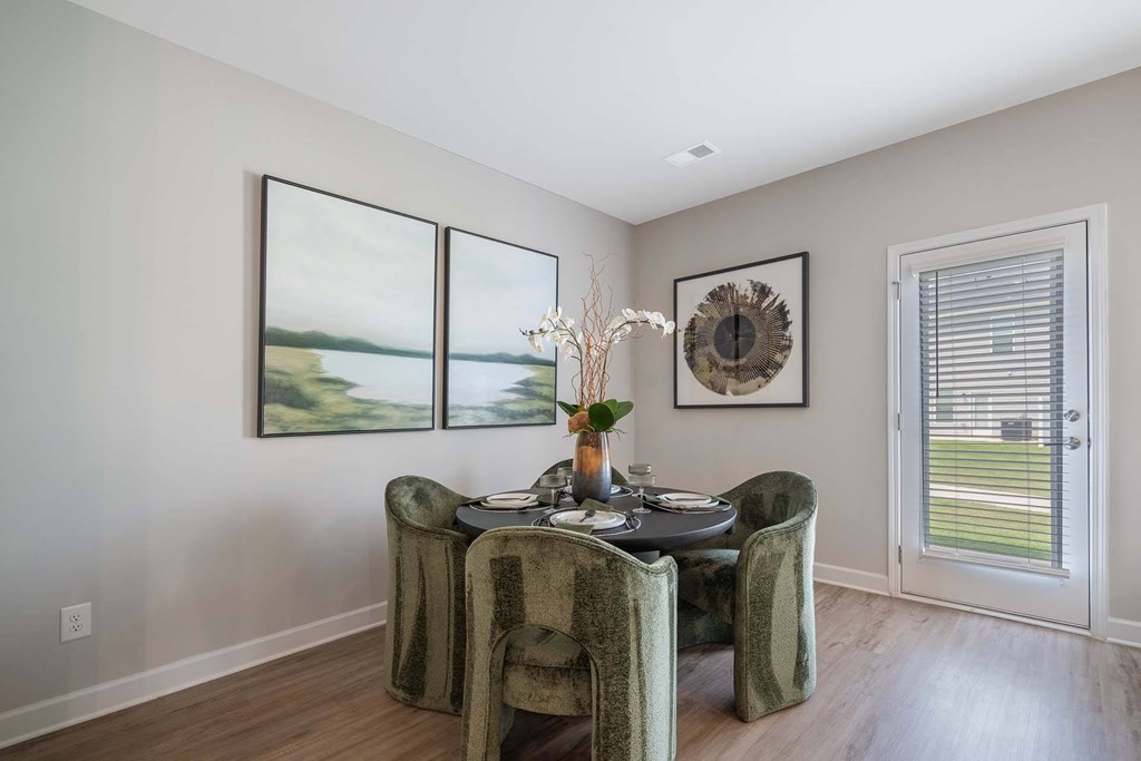 A dining room with a table set for two and a view of the outdoors through the window.