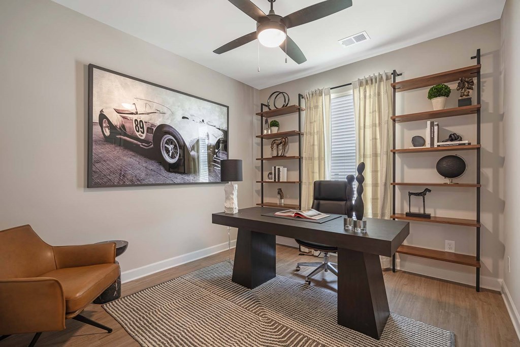 A room with a brown chair, a desk, and a painting of a vintage car on the wall.