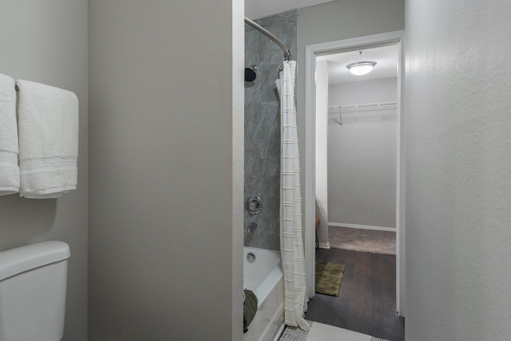 A bathroom with a toilet, a shower curtain, and a doorway leading to another room.