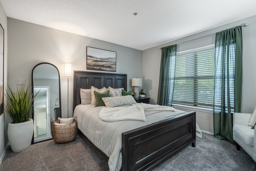 A bedroom with a large bed, a mirror, a potted plant, and a painting on the wall.