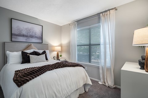 A bedroom with a large bed and a window with white curtains.
