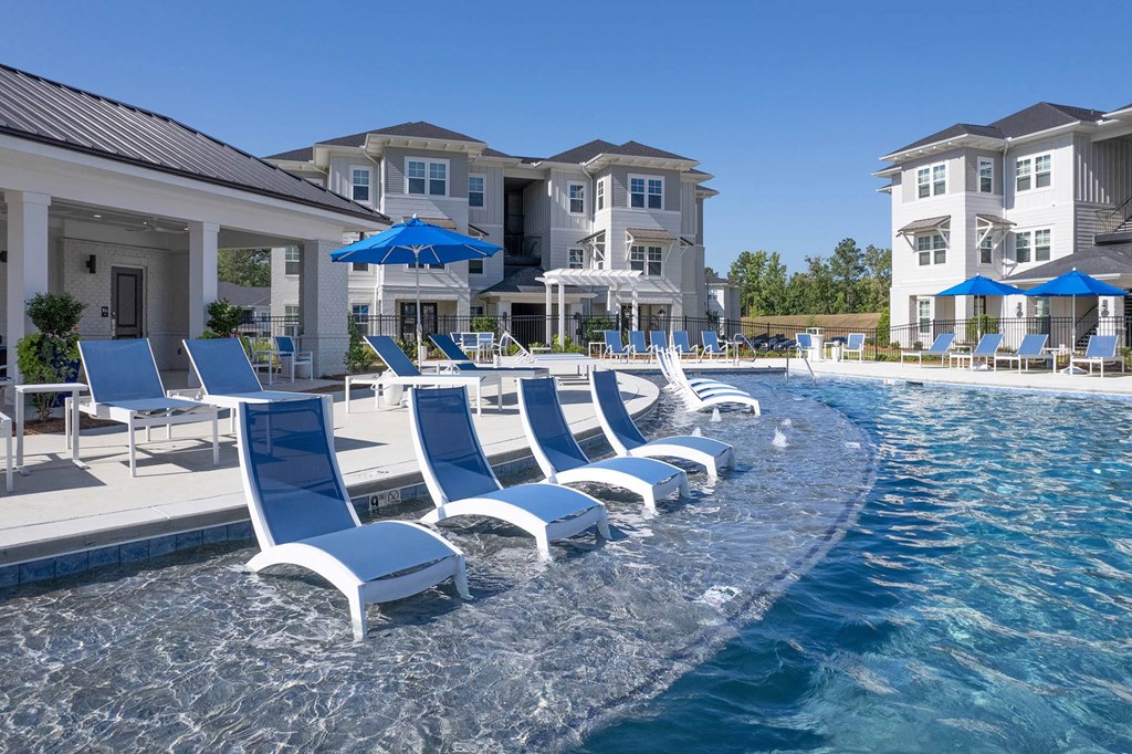 a row of blue lounge chairs in a pool with a building in the background