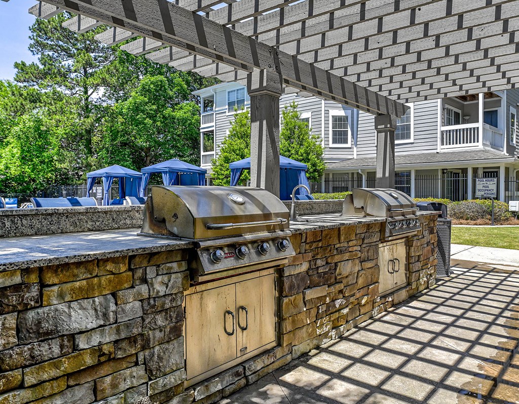 an outdoor kitchen with two bbq grills and a stone wall