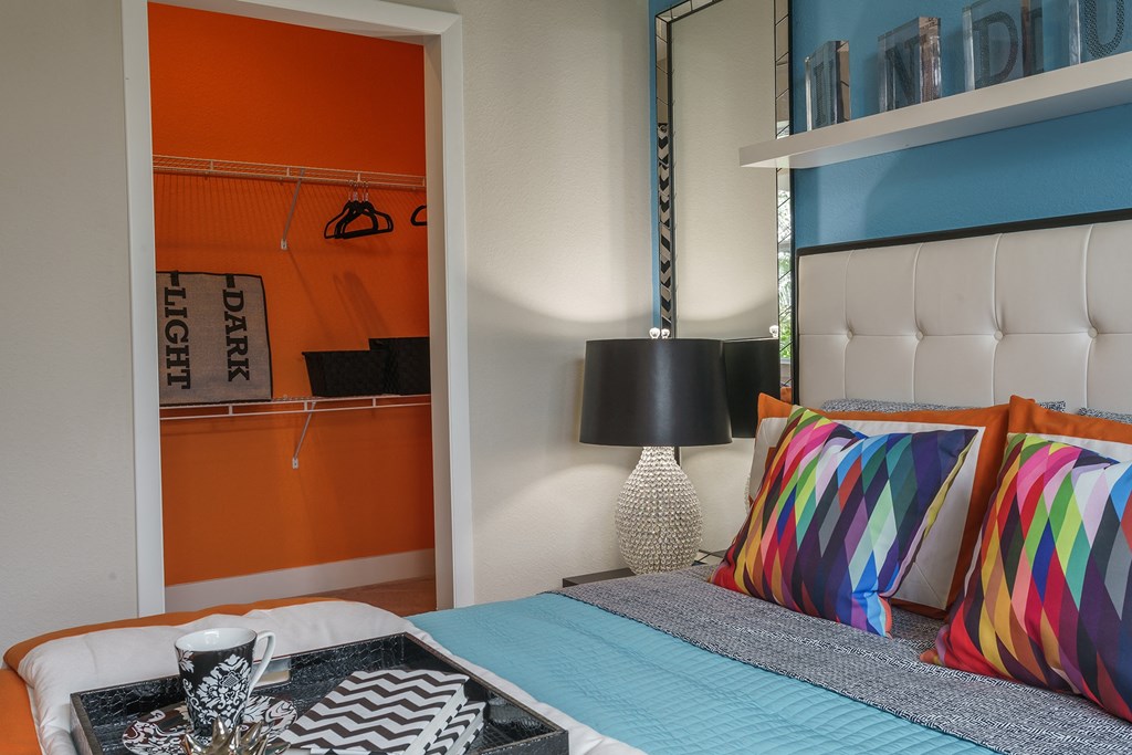 a bedroom with a bed with colorful pillows and a table with a lamp