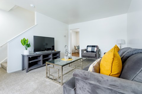 A living room with a grey couch and a glass coffee table.