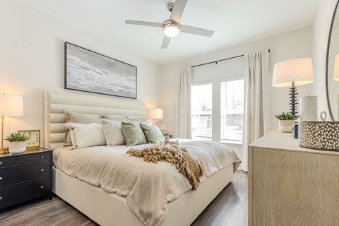 A bedroom with a large bed, a ceiling fan, and a nightstand with a lamp.