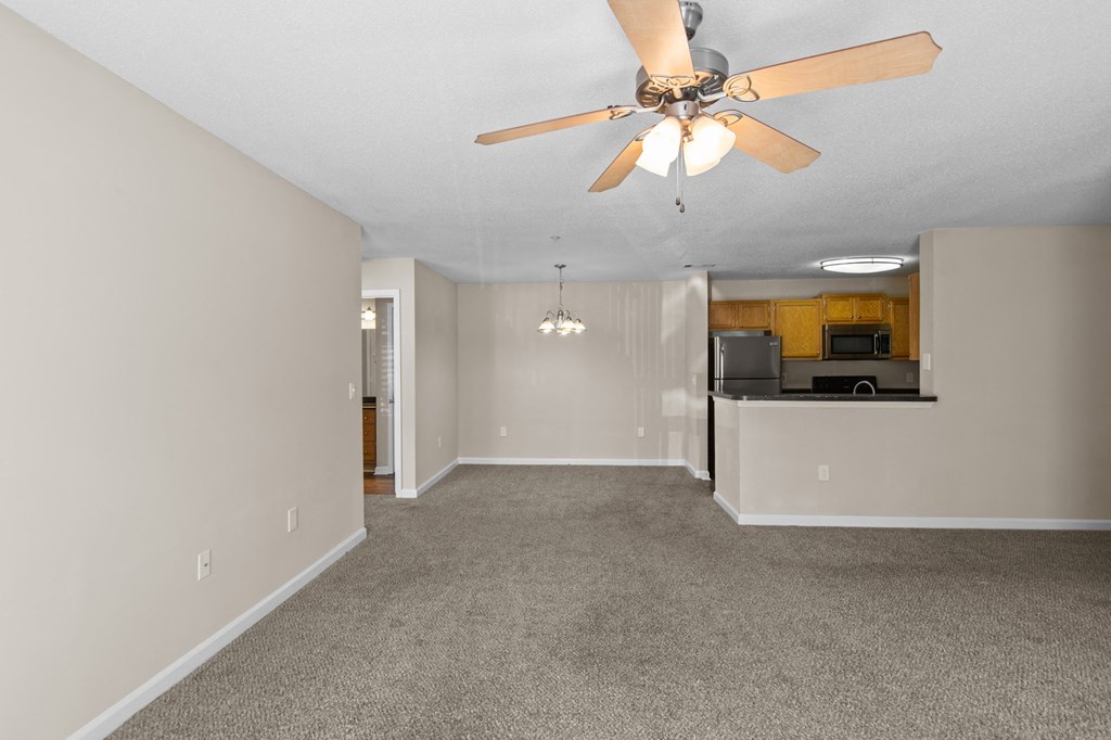an empty living room with a ceiling fan and a kitchen