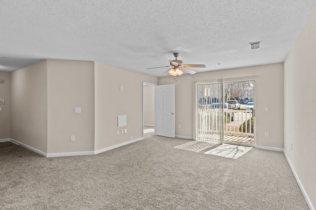 an empty living room with a ceiling fan and a door to a balcony