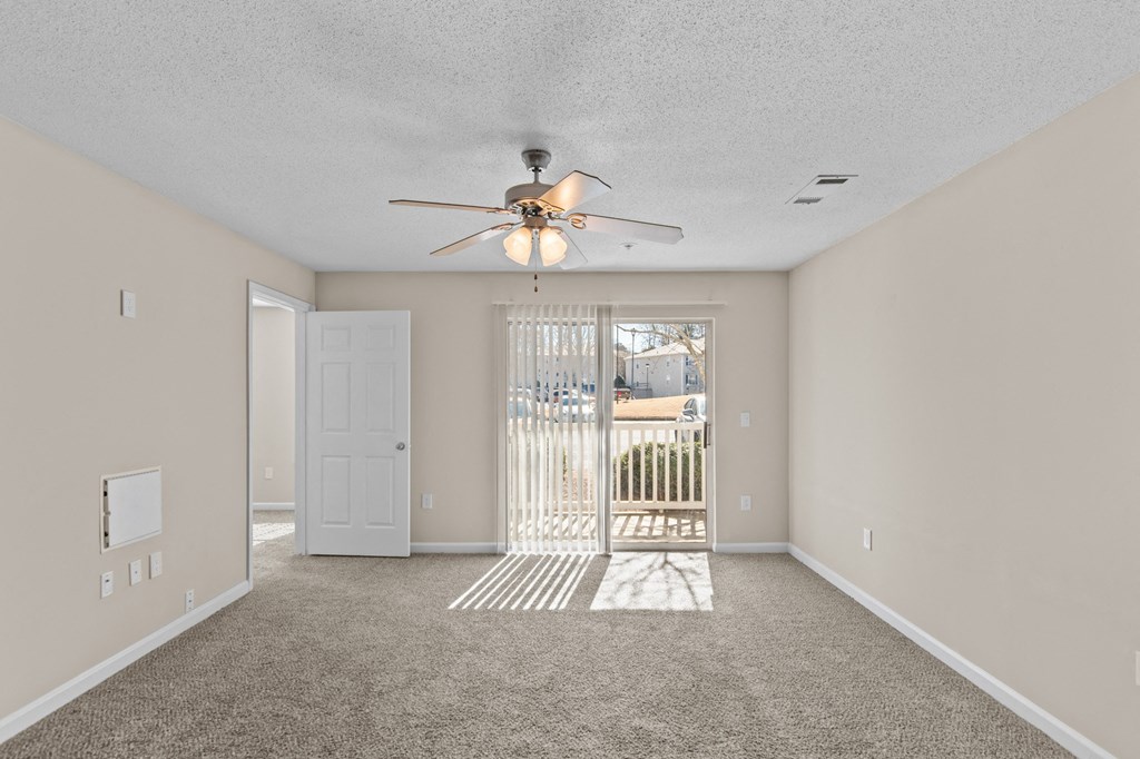 an empty living room with a ceiling fan and a door to a balcony