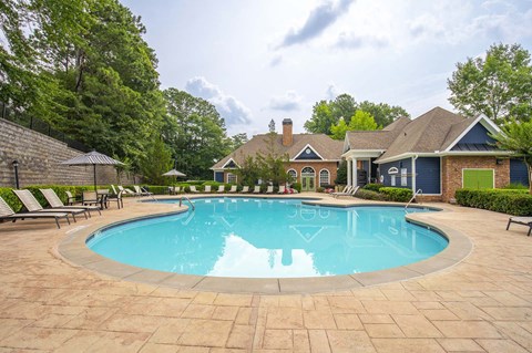 A large swimming pool surrounded by a brick patio and lounge chairs.