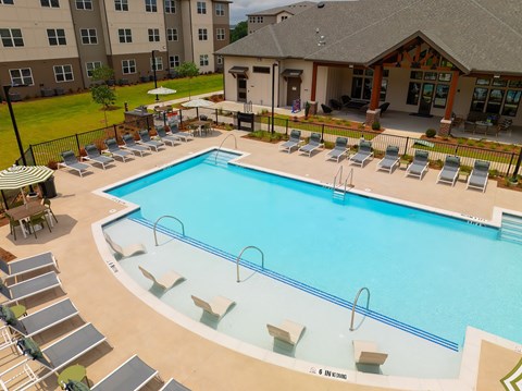 A large outdoor swimming pool surrounded by sun loungers and a building in the background.