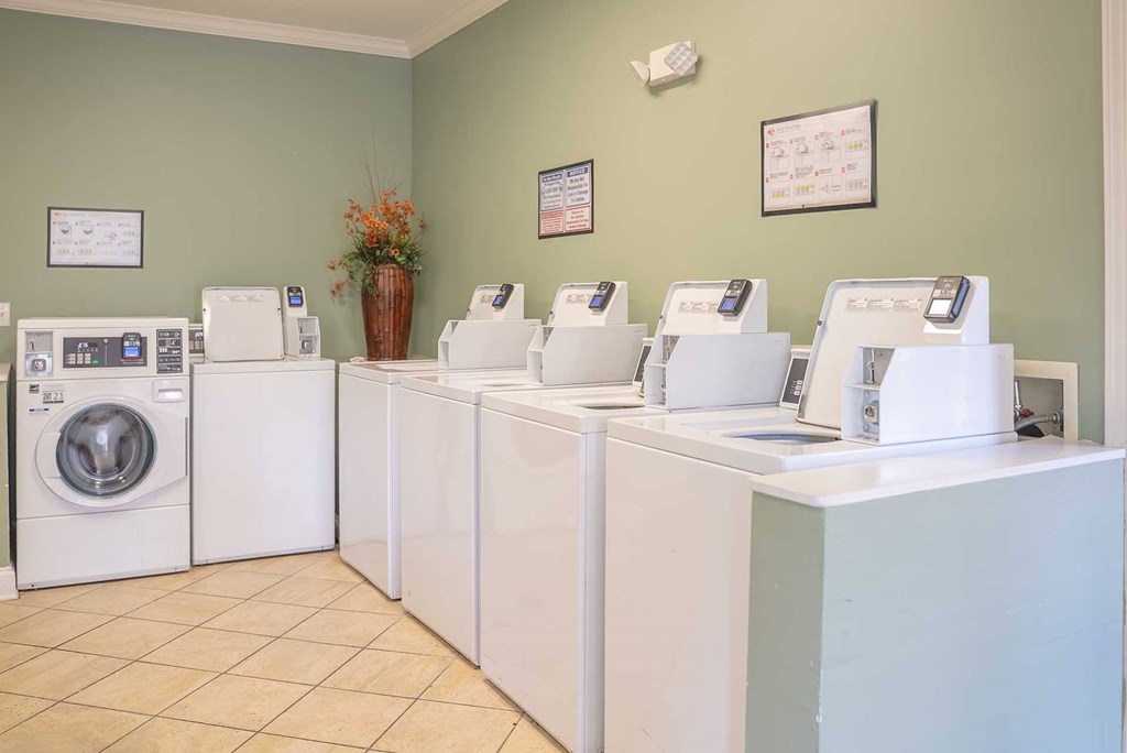 A laundromat with a green wall and a row of washers and dryers.