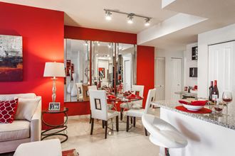 a dining room with a red accent wall and white chairs at Altis Kendall Square, Miami, 33196