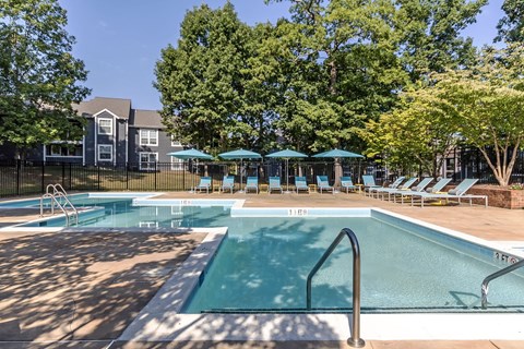 A swimming pool surrounded by trees and chairs.