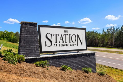 A sign that says "The Station at Lenoir City" is displayed in front of a road.