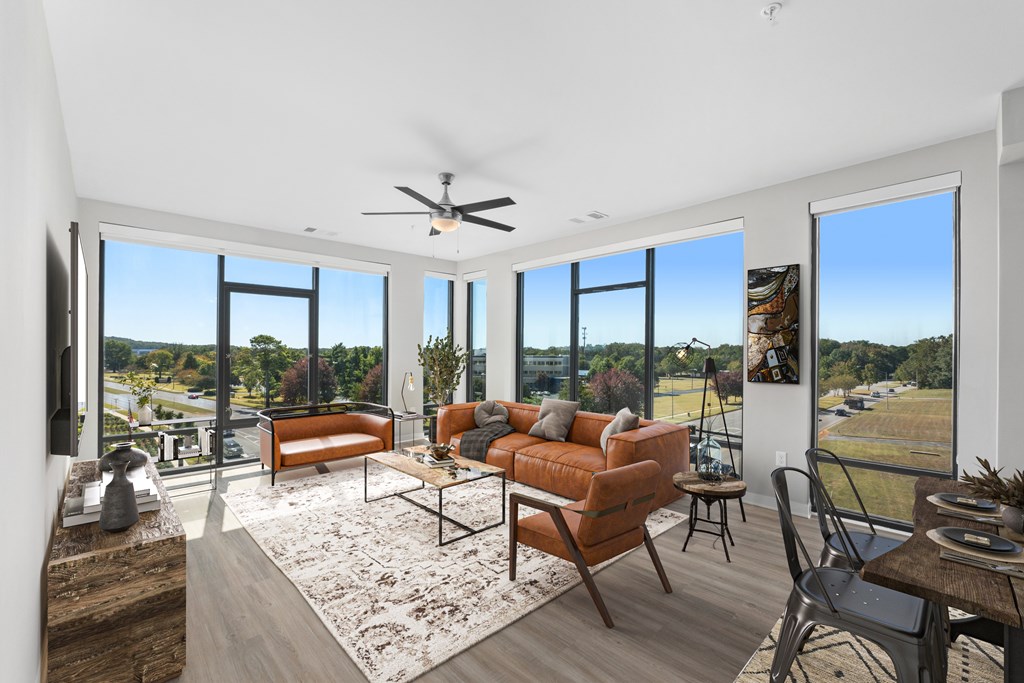 Huntsville, Al Luxury Apartments for Rent - The Arcadia - Living Room with Luxury Vinyl Plank Flooring, Area Rug, Sofa, Two-Seater Settee, Armchair, Coffee Table, Media Cabinet, Wall-Mounted TV, 9-foot Ceiling, Ceiling Fan, and Floor-to-Ceiling Windows with Expansive Views.