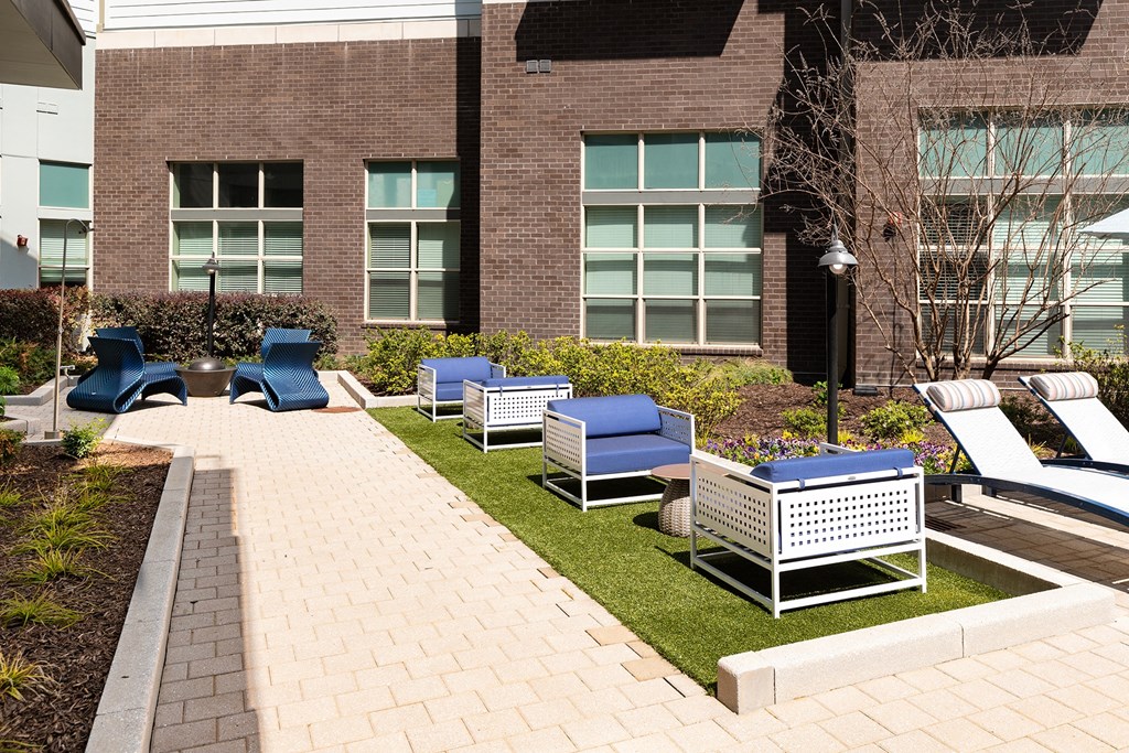 an outdoor lounge area with chairs and tables in front of a building
